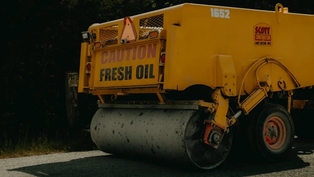 Vintage yellow Scott Construction fresh oil application truck with large roller drum, parked at dusk with Scott Construction branding visible on tank.